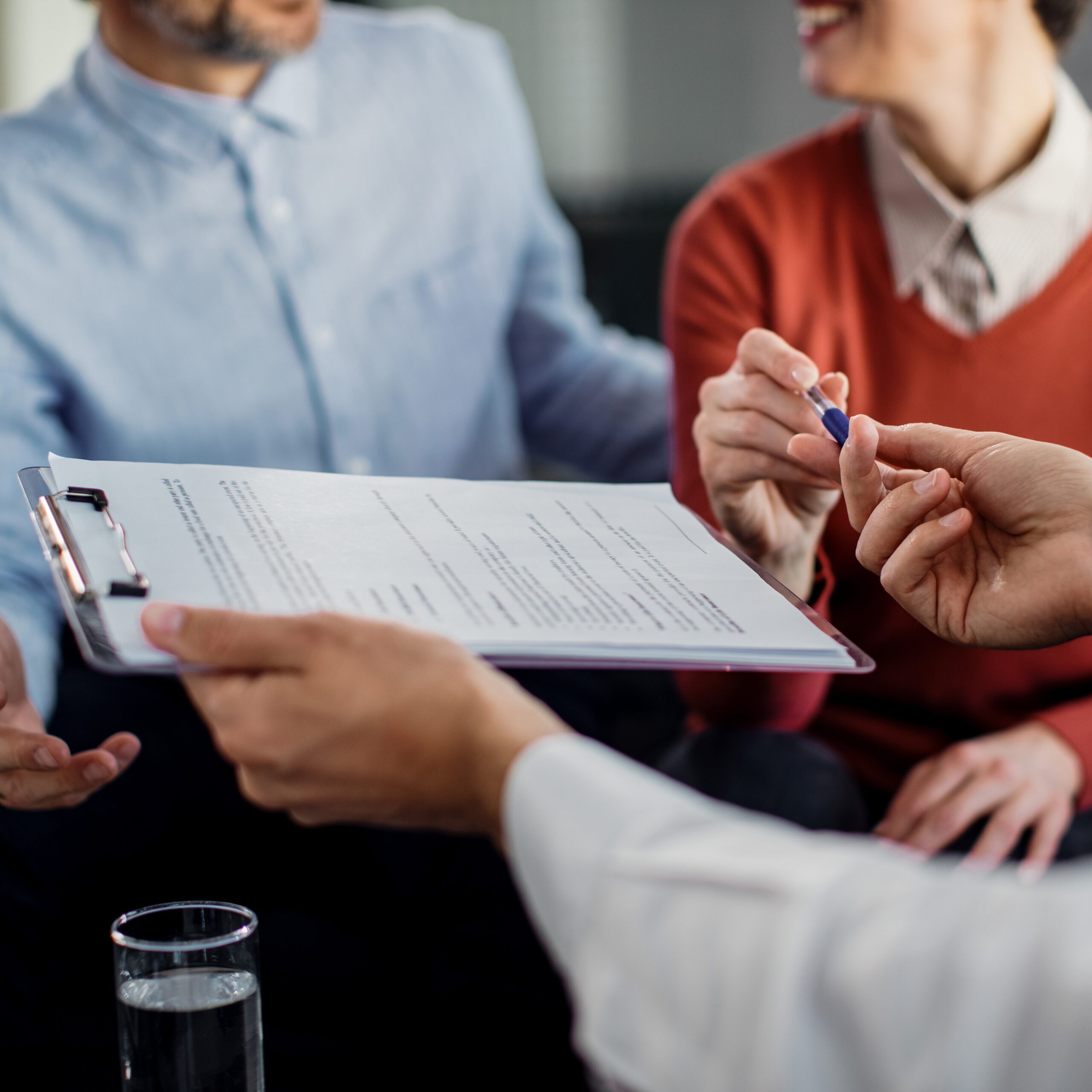 Close-up of unrecognizable couple signing a contract with financial advisor. Signature d’un contrat d’assurance sur une table avec des documents officiels et un stylo